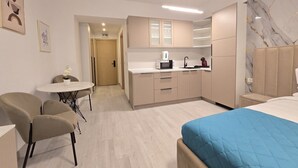Ein modernes Hotelzimmer mit Bett, einer kleinen Küchenzeile, einem Essbereich mit Tisch und Stühlen sowie einem Badezimmer.