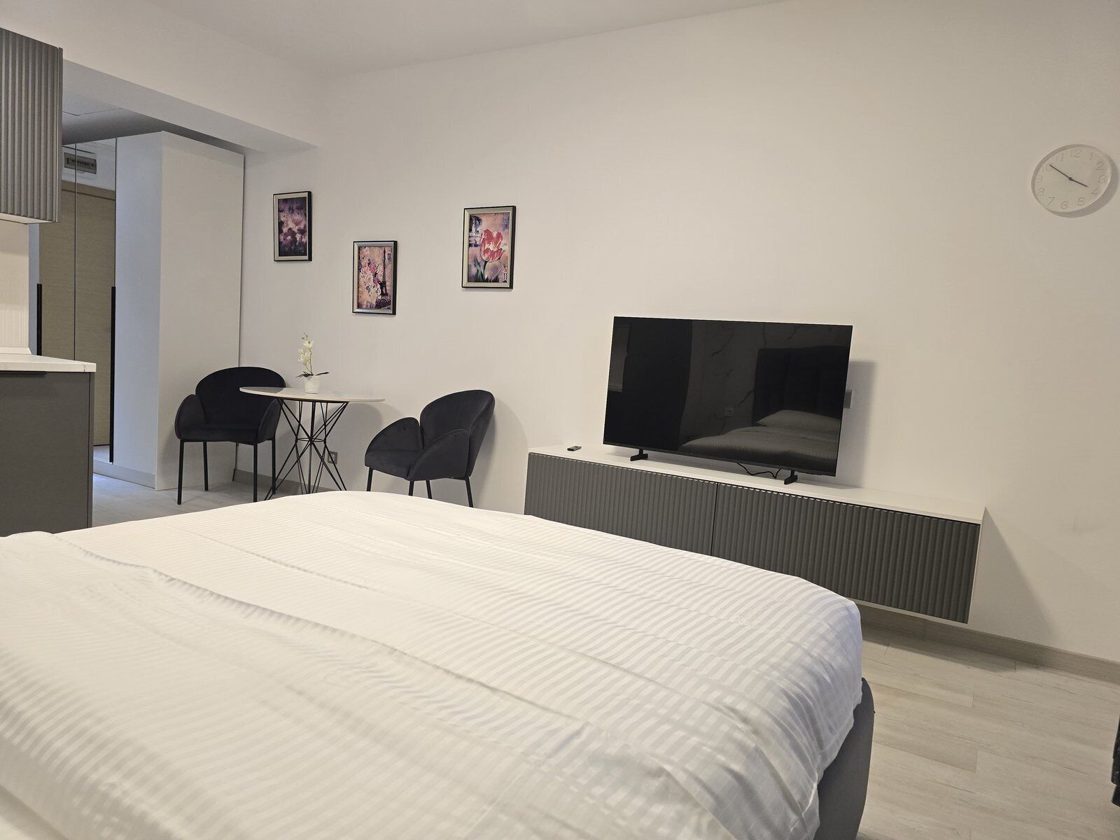 Moderni hotellihuone, jossa on suuri sänky, seinälle asennettu televisio sekä pieni pöytä ja kaksi tuolia.