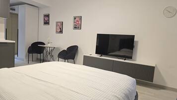 Moderni hotellihuone, jossa on suuri sänky, seinälle asennettu televisio sekä pieni pöytä ja kaksi tuolia.