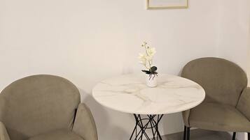 A room with a round marble table, two beige chairs, and two framed artworks on the wall.