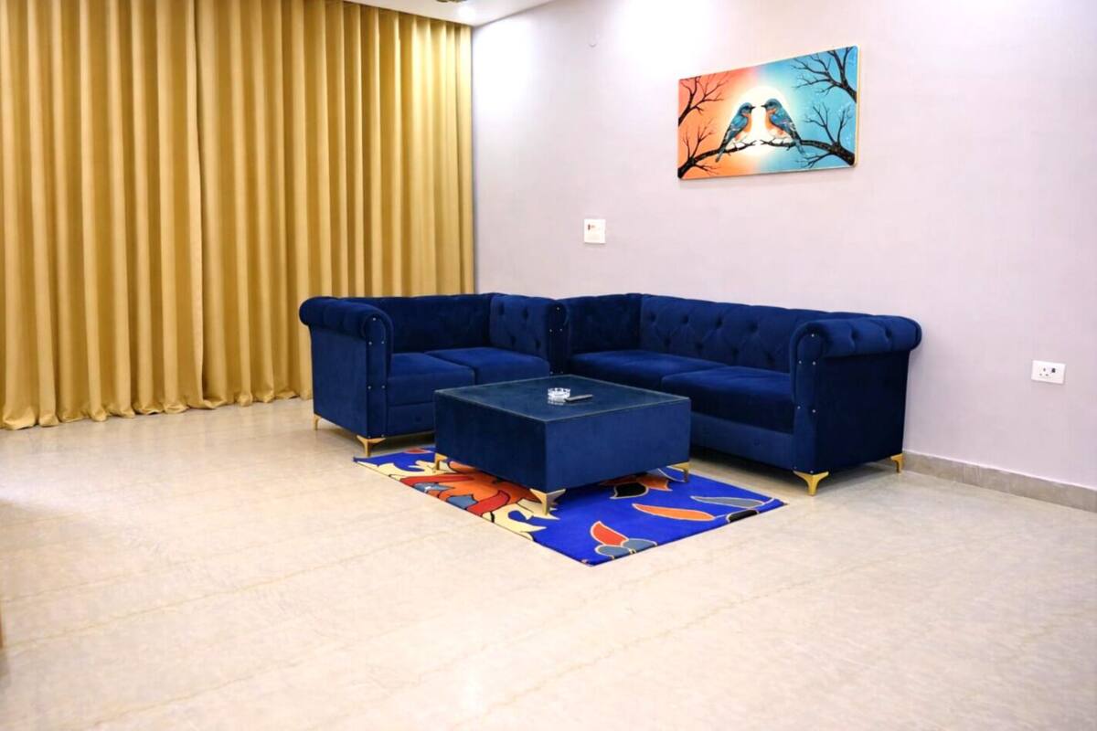 A room with a blue sectional sofa, a glass coffee table, and a colorful rug.