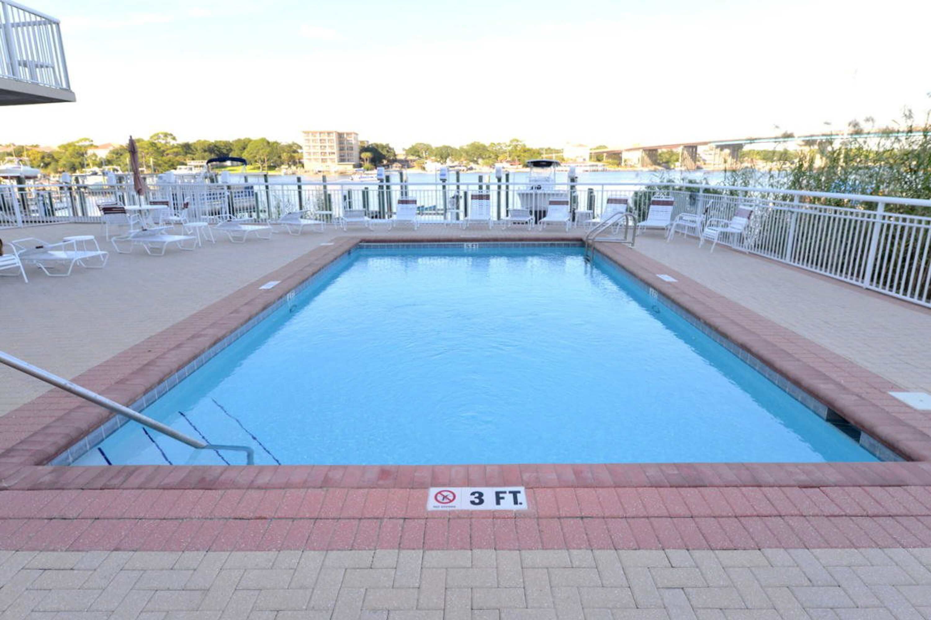Une piscine rectangulaire dont la profondeur est indiquée par un panneau indiquant 3 pieds, entourée de chaises longues blanches et d’une rambarde en métal.