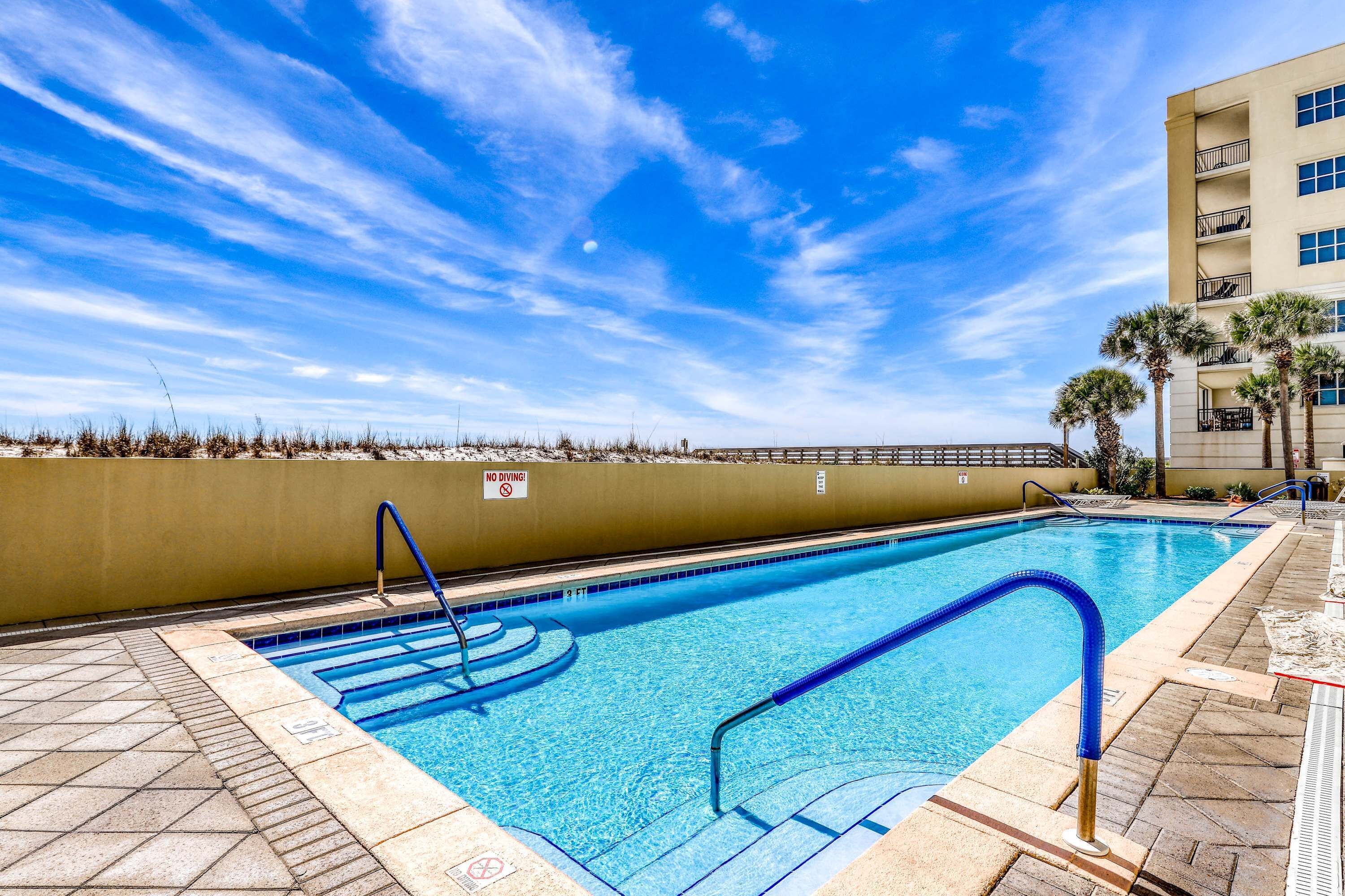Una piscina con azulejos azules, un cartel de prohibido bucear y un cielo despejado.