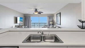 A modern kitchen with a dual sink, a ceiling fan, and a view of the balcony. - Gulf front home with shared pool, private balcony and beach access (Fort Walton Beach)