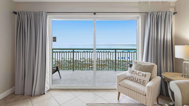 A room with a view of the beach, a sliding glass door, a striped armchair, and a small table with a lamp. - Gulf front home with shared pool, private balcony and beach access (Fort Walton Beach)