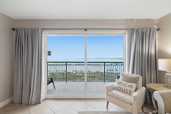 A room with a view of the beach, a sliding glass door, a striped armchair, and a small table with a lamp. - Gulf front home with shared pool, private balcony and beach access (Fort Walton Beach)