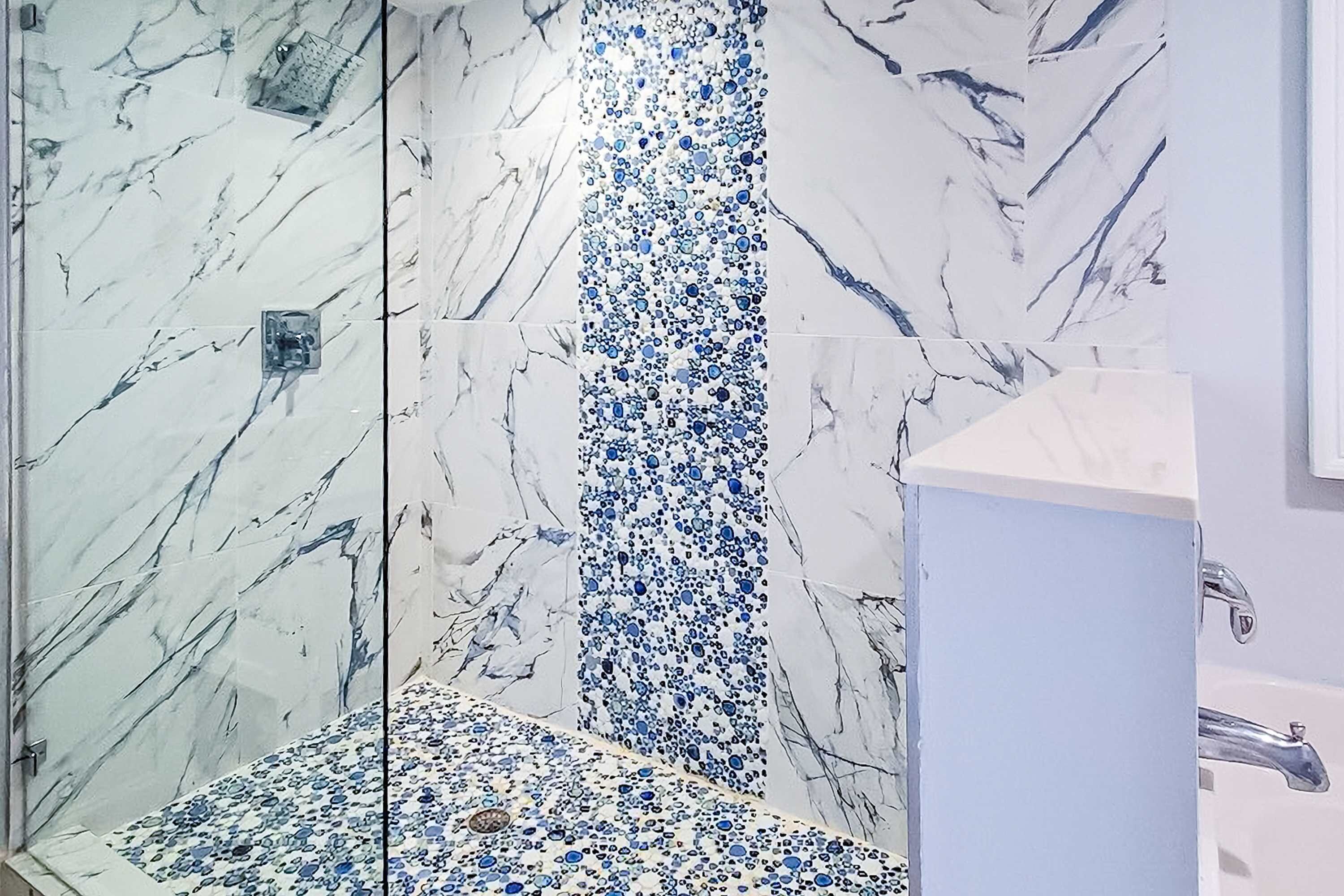 A bathroom with a marble shower wall and a sink with a modern faucet.