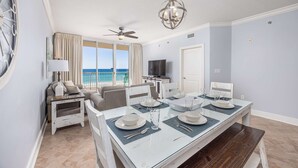 Uma sala de jantar com mesa posta para quatro pessoas, um ventilador de teto e vista para o mar.