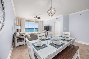 A dining area with a table set for four, a ceiling fan, and a view of the ocean. - 5th Floor Condo with Pools Onsite, Nearby Activities, Shops, Restaurants (Fort Walton Beach)