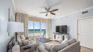 Uma sala de estar moderna com TV de tela plana, ventilador de teto e vista para o oceano por meio de amplas portas deslizantes.