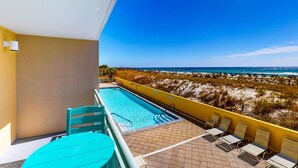 Ein Balkon mit Pool, Stühlen und Blick auf Strand und Meer.