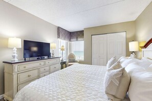 A hotel room with a large bed, a dresser with a TV, and two lamps. - Beachfront Condo with stunning views, shared pool and beach access (Fort Walton Beach)