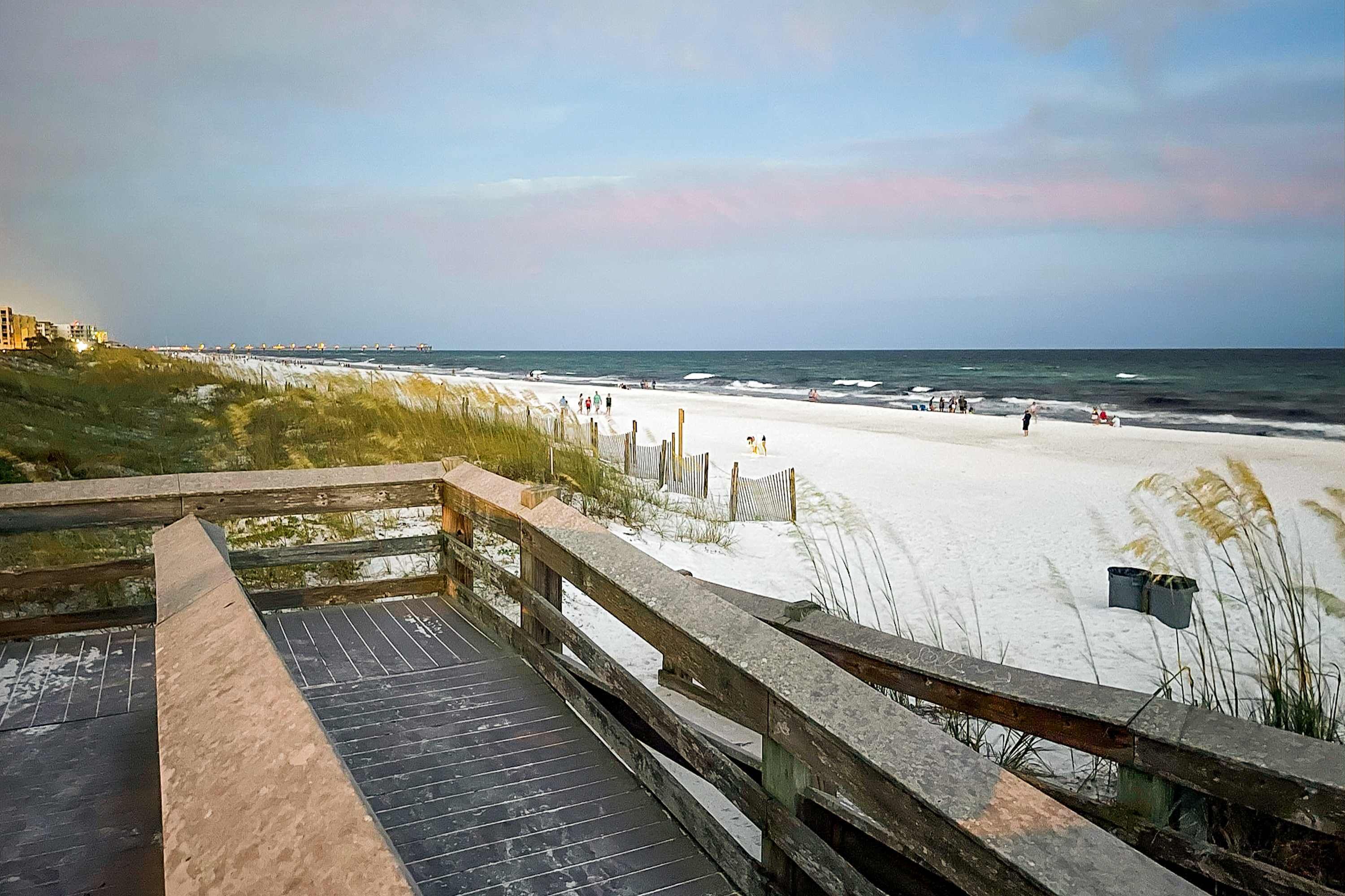 A wooden boardwalk leading to a beach with a sandy shore and ocean view.