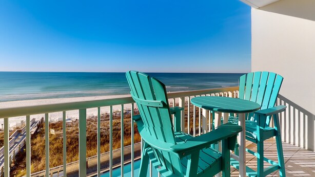 Un balcon avec deux fauteuils Adirondack verts et une petite table, donnant sur une plage et l’océan.