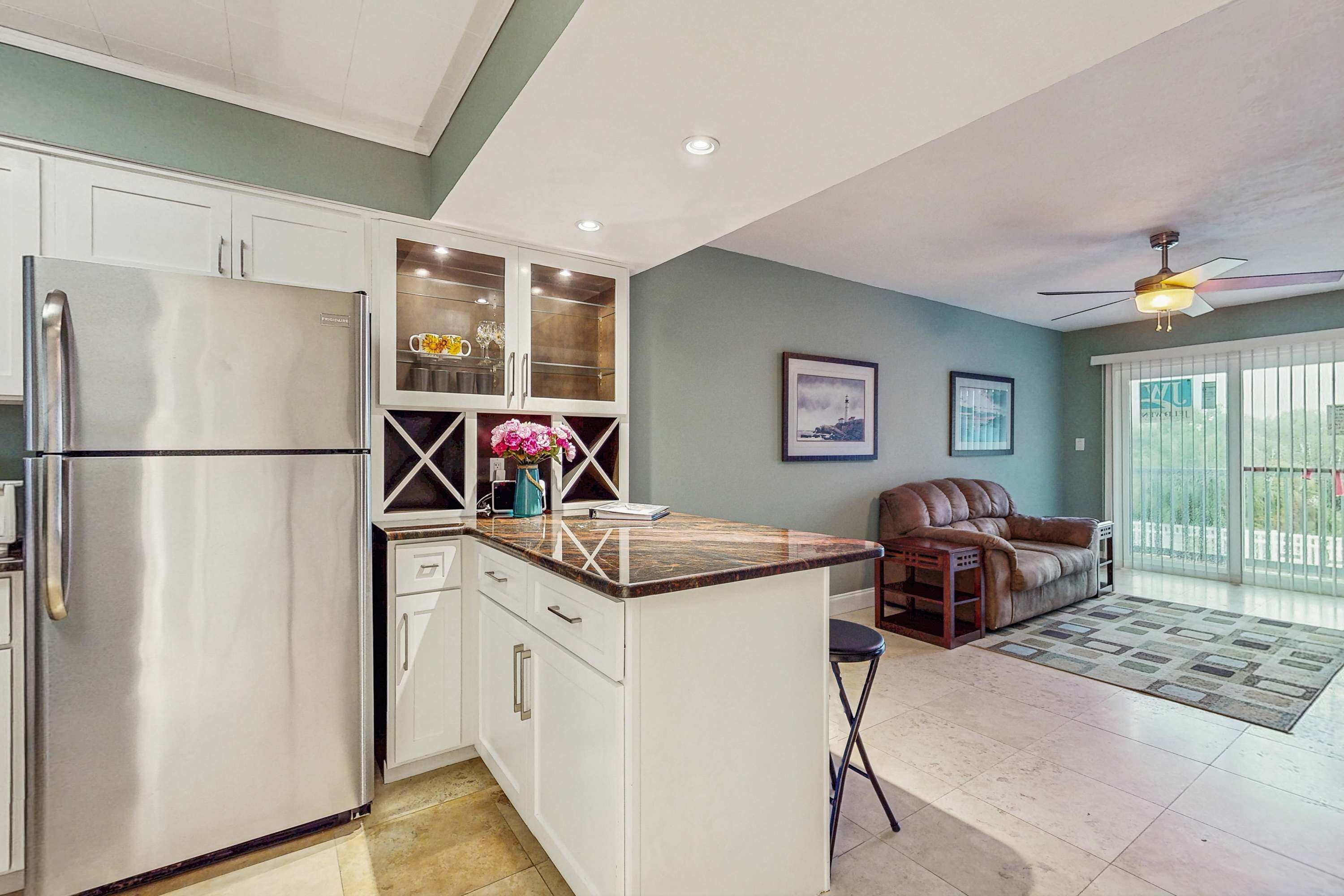 A modern kitchen with white cabinetry, a stainless steel refrigerator, and a marble countertop island.