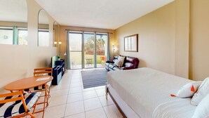 A hotel room with a bed, a desk with a chair, a sofa, and a large window. - Serene studio with garden-level patio, central AC, waterfront pool & marina (Fort Walton Beach)