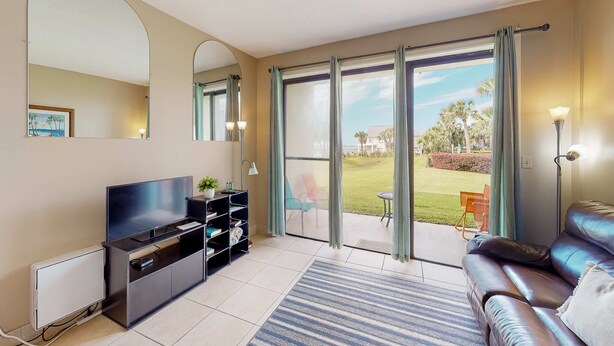 A modern living room with a flat-screen TV, a sofa, a coffee table, and a sliding glass door leading to a patio with outdoor furniture. - Serene studio with garden-level patio, central AC, waterfront pool & marina (Fort Walton Beach)