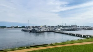 A marina with boats docked, a grassy area in the foreground, and a cityscape in the background. - Serene studio with garden-level patio, central AC, waterfront pool & marina (Fort Walton Beach)