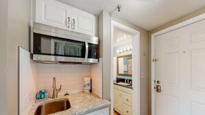 A kitchen with white cabinets, a stainless steel microwave, a sink, and a door leading to another room. - Serene studio with garden-level patio, central AC, waterfront pool & marina (Fort Walton Beach)