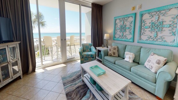 A living room with a sofa, a coffee table, a TV, and a view of the ocean through large sliding doors. - Gorgeous beachfront condo w/ocean views, shared pool, and beach access (Fort Walton Beach)