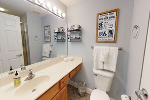 A bathroom with a sink, mirror, and toilet. There are shelves with toiletries and a sign with bathroom rules. - Gorgeous beachfront condo w/ocean views, shared pool, and beach access (Fort Walton Beach)