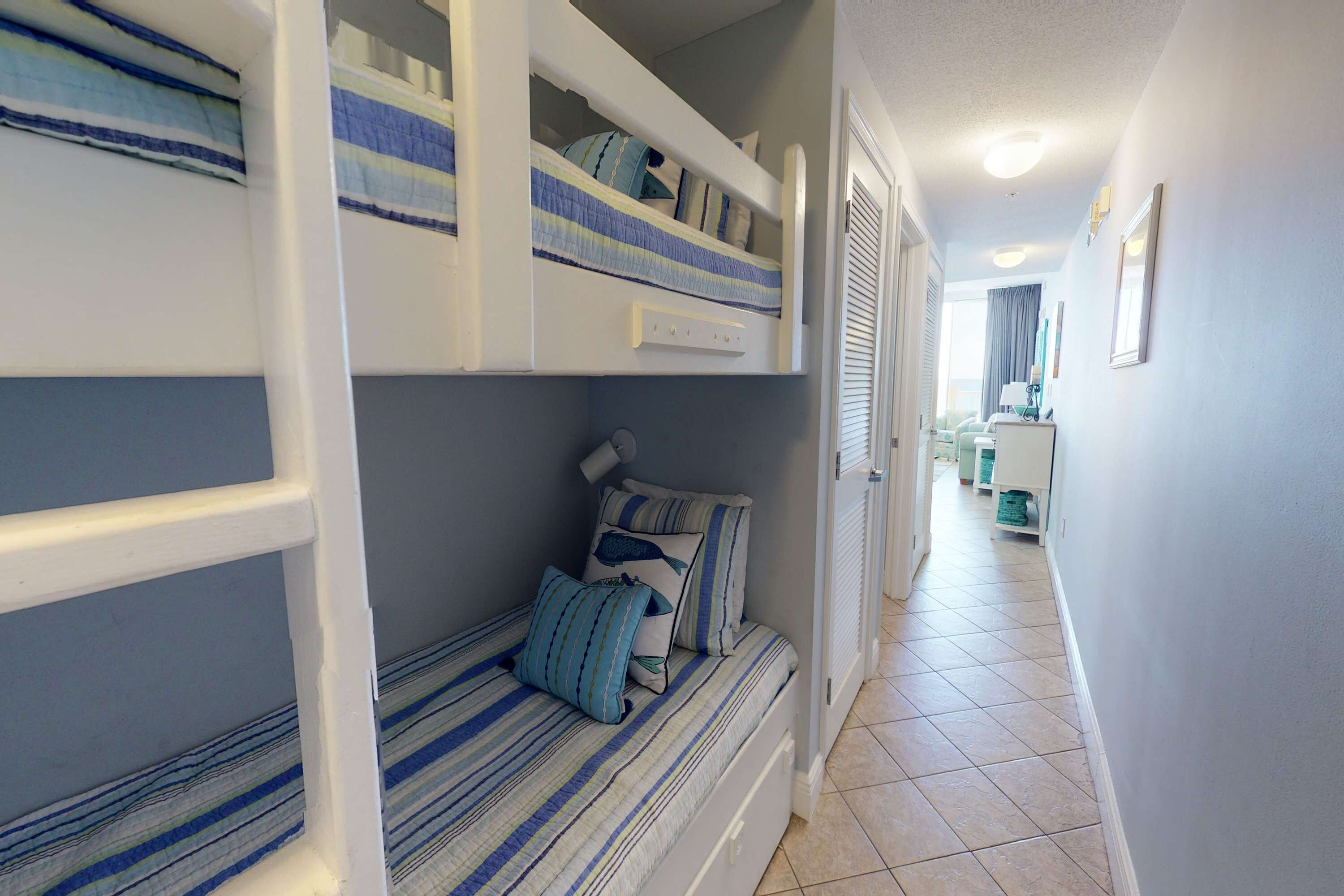 Une chambre avec un lit superposé, une couette à rayures, une table de chevet et une lampe.