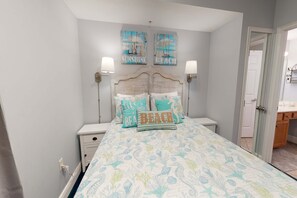 A bedroom with a bed, two wall-mounted lamps, and two framed pictures on the wall. - Gorgeous beachfront condo w/ocean views, shared pool, and beach access (Fort Walton Beach)