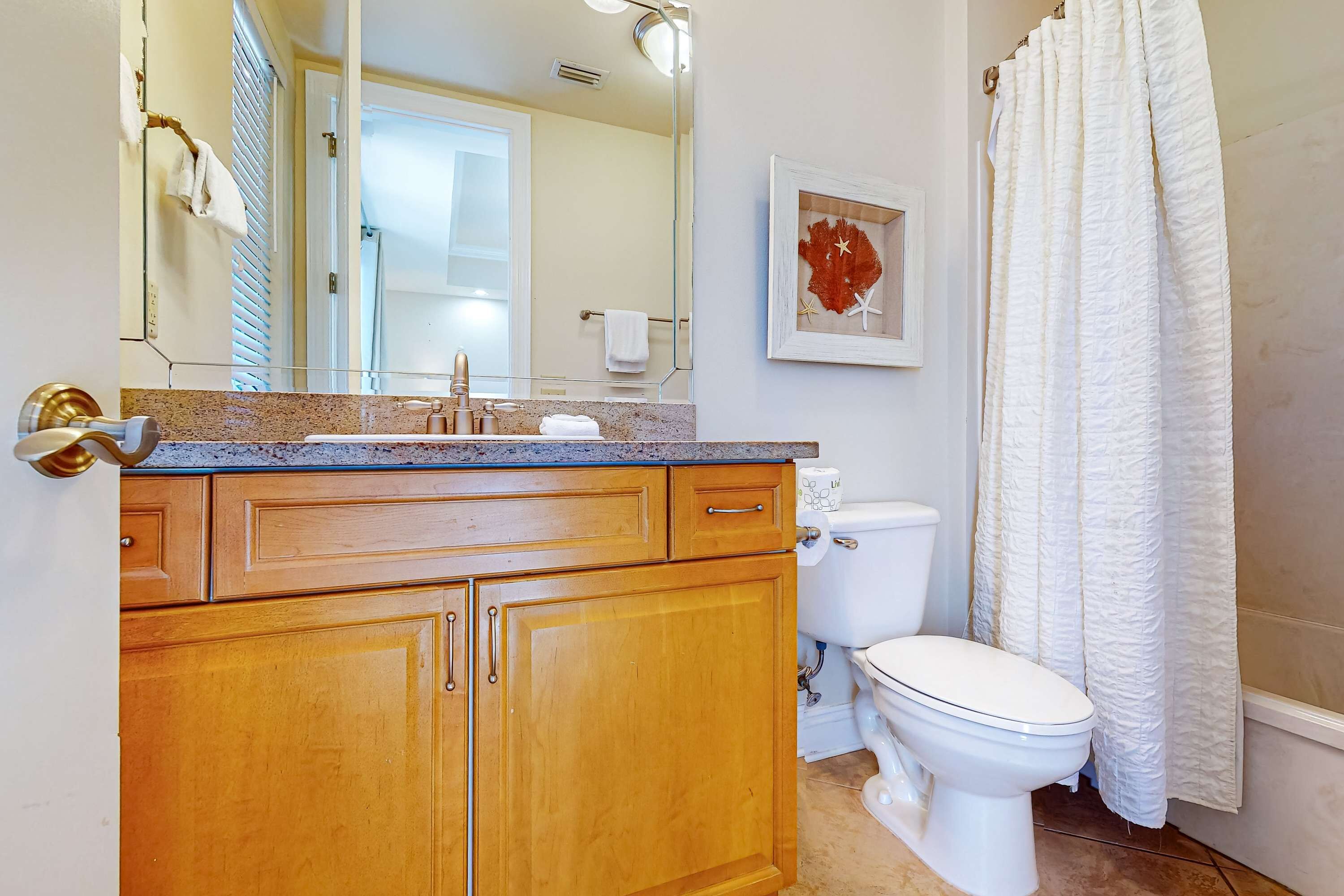 A bathroom with wooden cabinets, a sink, a toilet, and a shower curtain.
