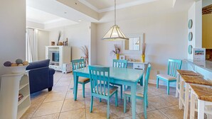 A dining area with a teal table and chairs, a sofa, and a TV in the background. - Stylish townhouse condo near the beach with full kitchen, WiFi, and shared pool (Santa Rosa Beach)