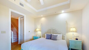 A bedroom with a large bed, two bedside tables with lamps, a wooden headboard, and a staircase leading to a closet. - Stylish townhouse condo near the beach with full kitchen, WiFi, and shared pool (Santa Rosa Beach)