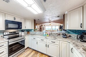Una cocina con gabinetes blancos, una estufa de acero inoxidable, un microondas y una cafetera.