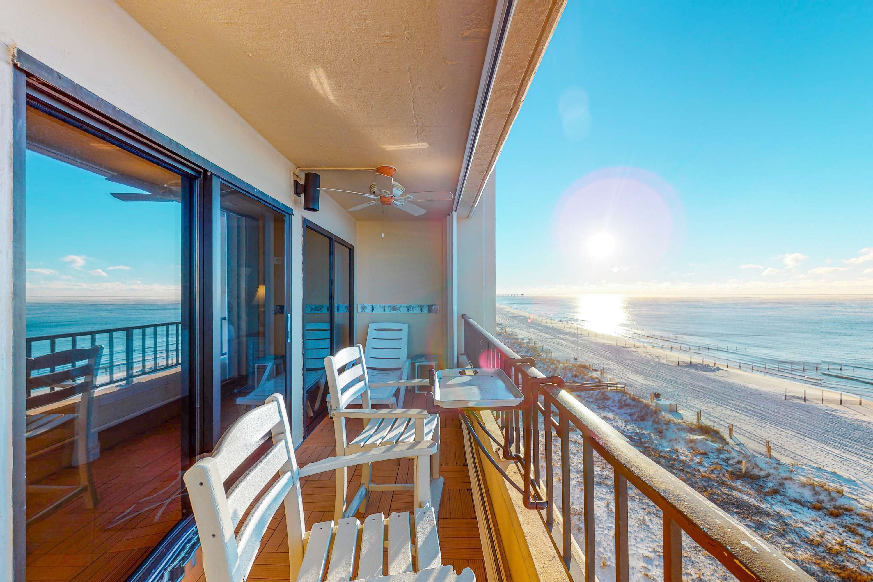 Un balcon avec vue sur la plage, une table, des chaises et un ventilateur de plafond.