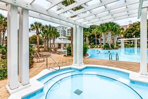 Un espace piscine agrémenté d’une pergola, de palmiers et de chaises longues.