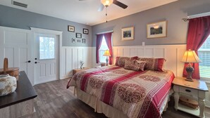 Ein Schlafzimmer mit einem großen Bett, einem Deckenventilator, einem Nachttisch und einem Fenster mit Vorhängen.