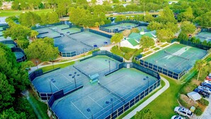 Eine Vogelperspektive auf einen Sportkomplex mit mehreren Tennisplätzen, umgeben von Grünflächen und Wohnhäusern.