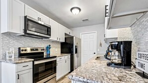 A modern kitchen with white cabinets, stainless steel appliances, a granite countertop, and a coffee station. - Dog-friendly townhome with private deck, charming interior, washer&dryer & AC (Gulf Breeze)