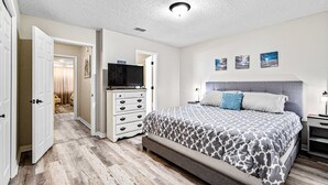 A bedroom with a bed, a dresser, a television, and a door leading to another room. - Dog-friendly townhome with private deck, charming interior, washer&dryer & AC (Gulf Breeze)