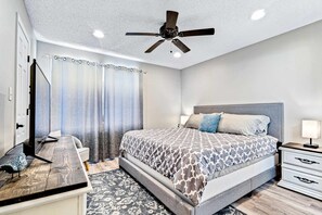 Une chambre à coucher comprenant un lit, des tables de chevet, un bureau, un ventilateur de plafond et une fenêtre avec des rideaux.
