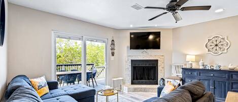 A living room with a fireplace, a ceiling fan, and a large TV.
