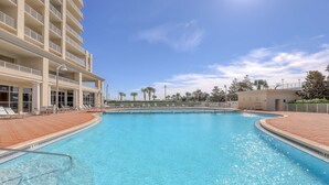 A swimming pool with a clear blue water, surrounded by a brick walkway, and adjacent to a multi-story building with balconies. - Seventh Floor Condo with Beach View Pool Gym and Private Balcony (Miramar Beach)