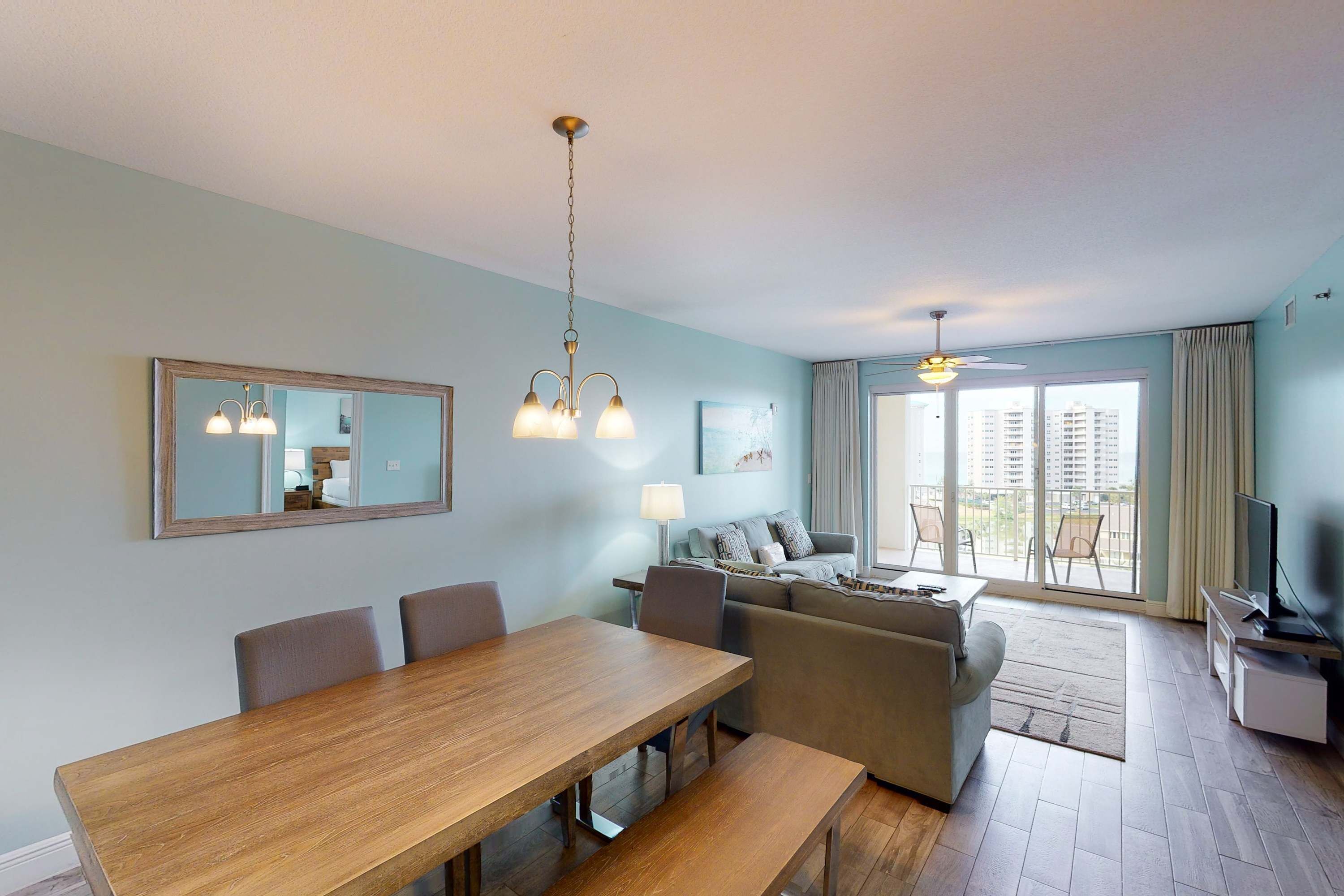 A modern living room with a dining area, a sofa set, a TV, and a balcony with a view of buildings.