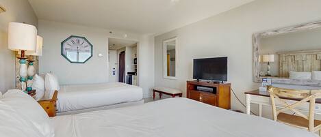 Habitación de hotel con dos camas, televisión, escritorio, silla, reloj y espejo.