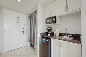 Een compacte keuken met witte kastjes, een ingebouwde magnetron, een koffiezetapparaat en een vaatwasser.
