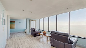 A spacious room with a large window, a sofa, a chair, and a wooden coffee table. - Bayside Studio with nearby outlet shopping, Golf course and Community pool (Miramar Beach)