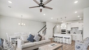 A modern living room with a sofa, coffee table, and a staircase leading to a kitchen area with bar stools. - The Townes #5145: Gorgeous New 4BR in Barefoot! With Driving Range Views! (North Myrtle Beach)
