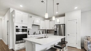 A modern kitchen with white cabinetry, stainless steel appliances, and a central island with bar stools. - The Townes #5145: Gorgeous New 4BR in Barefoot! With Driving Range Views! (North Myrtle Beach)