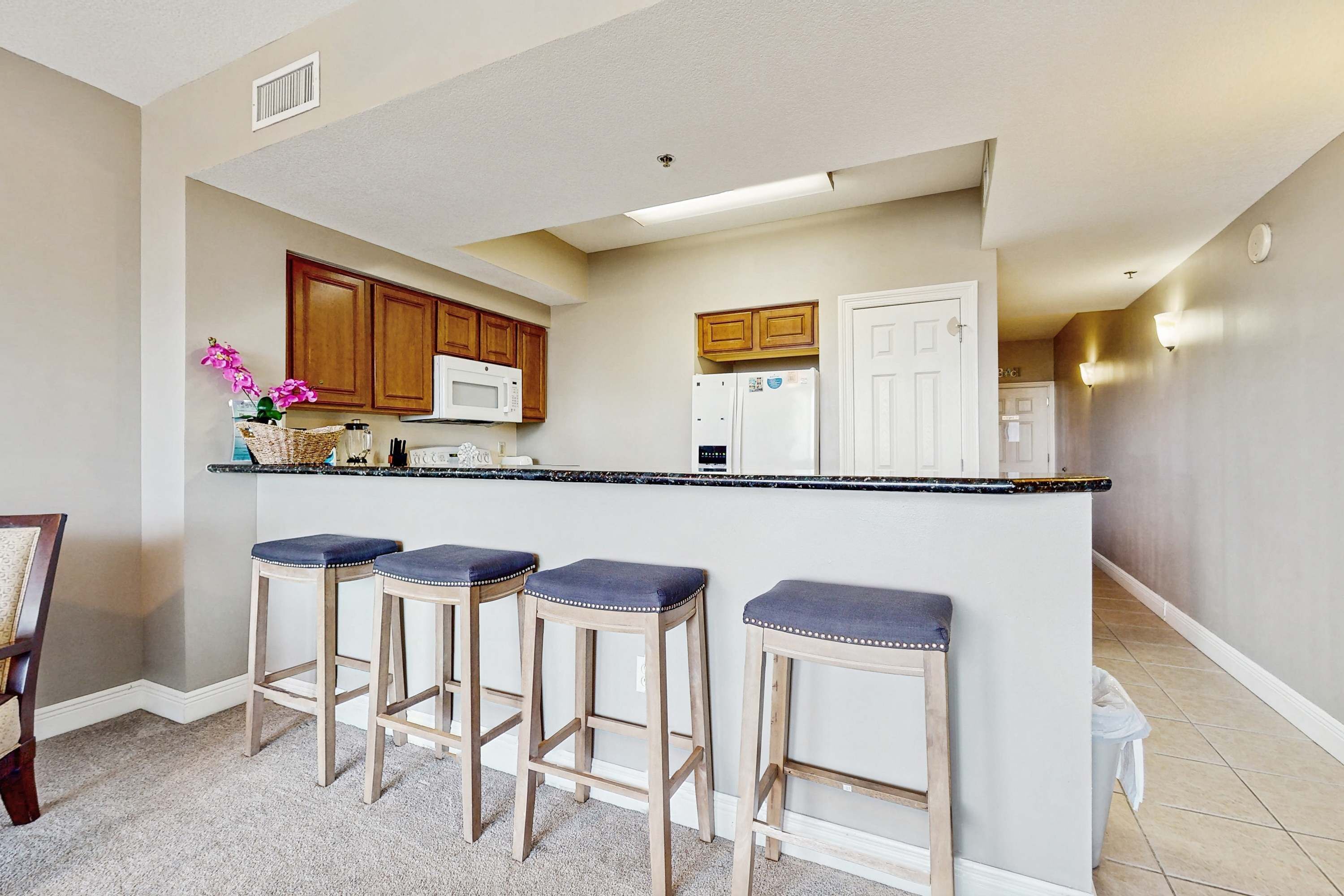 A kitchen with wooden cabinets, a white refrigerator, a microwave, and three bar stools.
