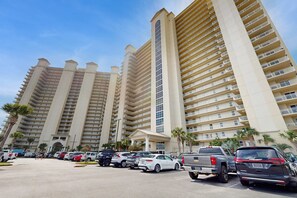 A multi-story hotel with a central atrium, parking lot, and palm trees. - Beachfront Condo with Pool Gym and Scenic Balcony in Miramar Beach (Miramar Beach)