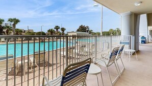 En balkon med udsigt til en swimmingpool, liggestole og et overdækket område med borde og stole.