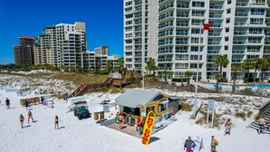 A beachside location with a lifeguard station, a pool, and high-rise buildings in the background. - Beautiful beachfront condo with pool, beach tram, tennis, golf, & on-site dining (Miramar Beach)